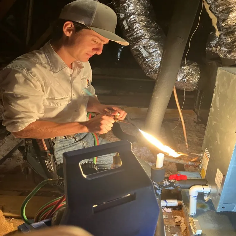 Technician brazing a copper refrigerant line in a Houston attic