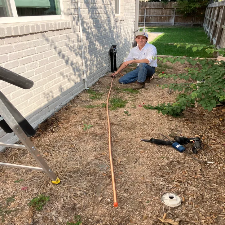 Technician running a new refrigerant line along the side of a home